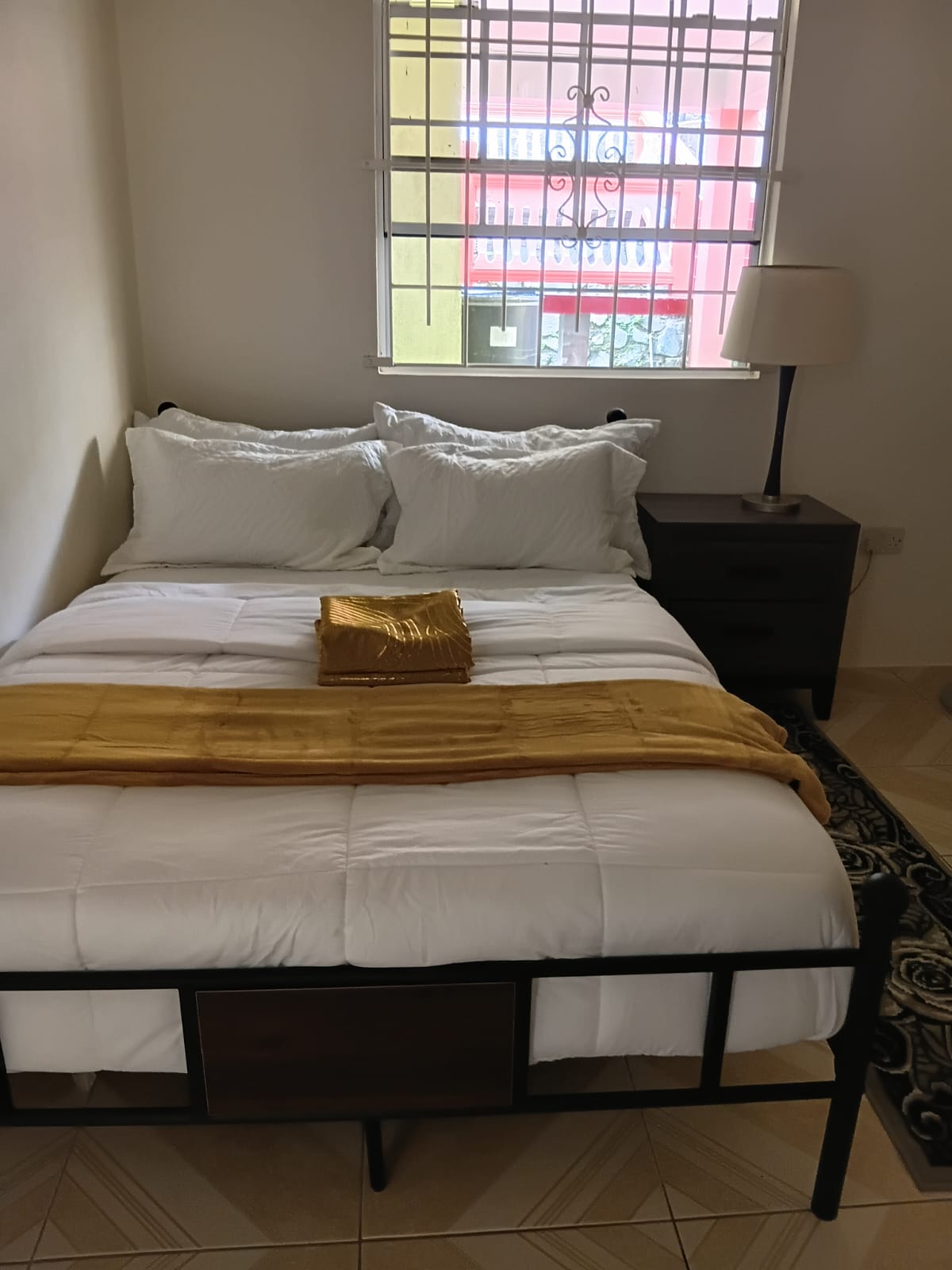 Second bedroom with a queen bed, white linens, bedside lamp and a window